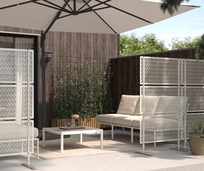 Two white metal privacy screens zoning off an outdoor seating area 