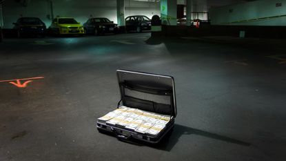 A briefcase full of money sits on the floor of a dimly lit parking garage.