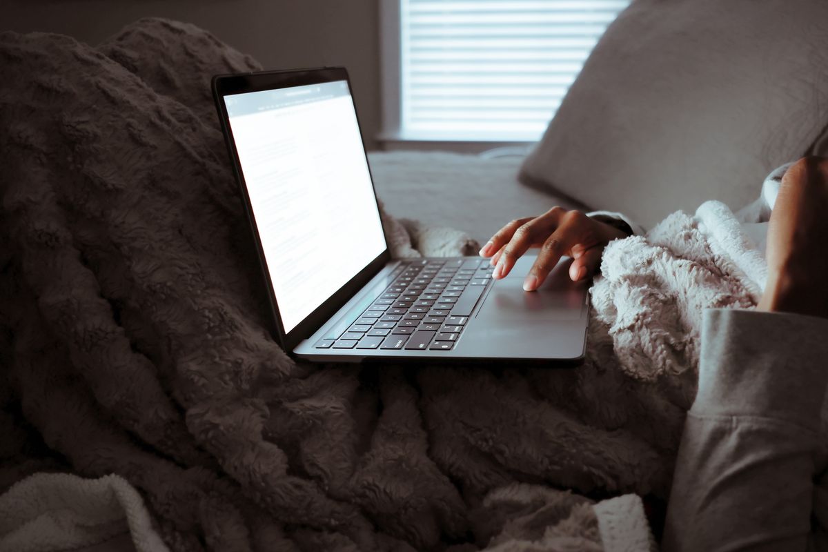 A woman sits in her bed at night with her laptop open on her lap.