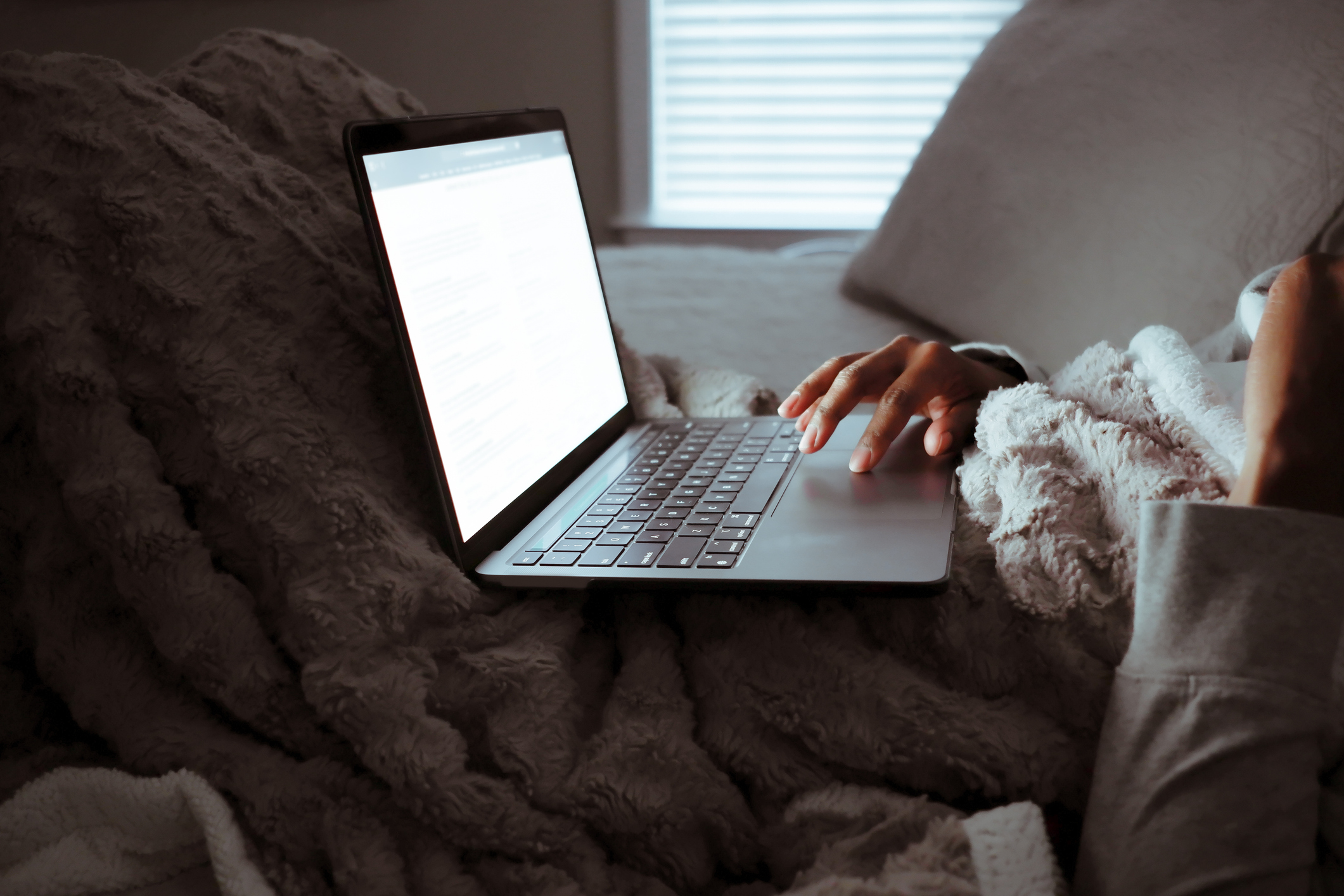 A woman sits in her bed at night with her laptop open on her lap.