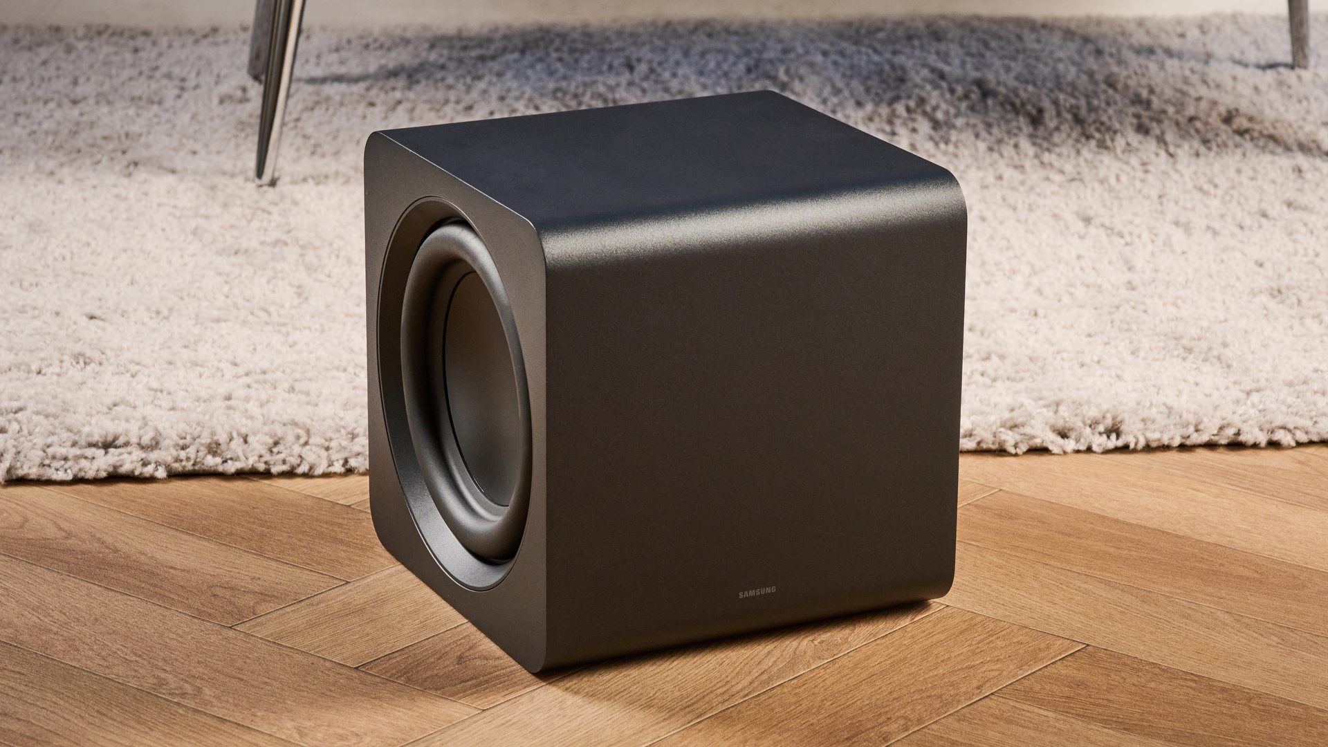 the samsung qs750f soundbar with two rear surround speakers and subwoofer photographed against a blue background and a TV