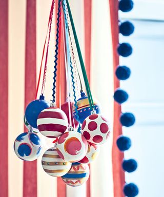 Decorated Christmas baubles hanging from ribbons in front of red and white striped curtains