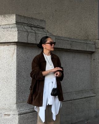 Woman wearing suede jacket, white shirt, white button-down around waist, and neutral-colored silk skirt.