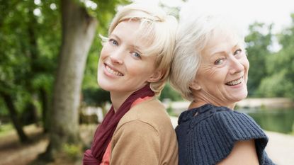 A senior mom and her adult daughter smile together.