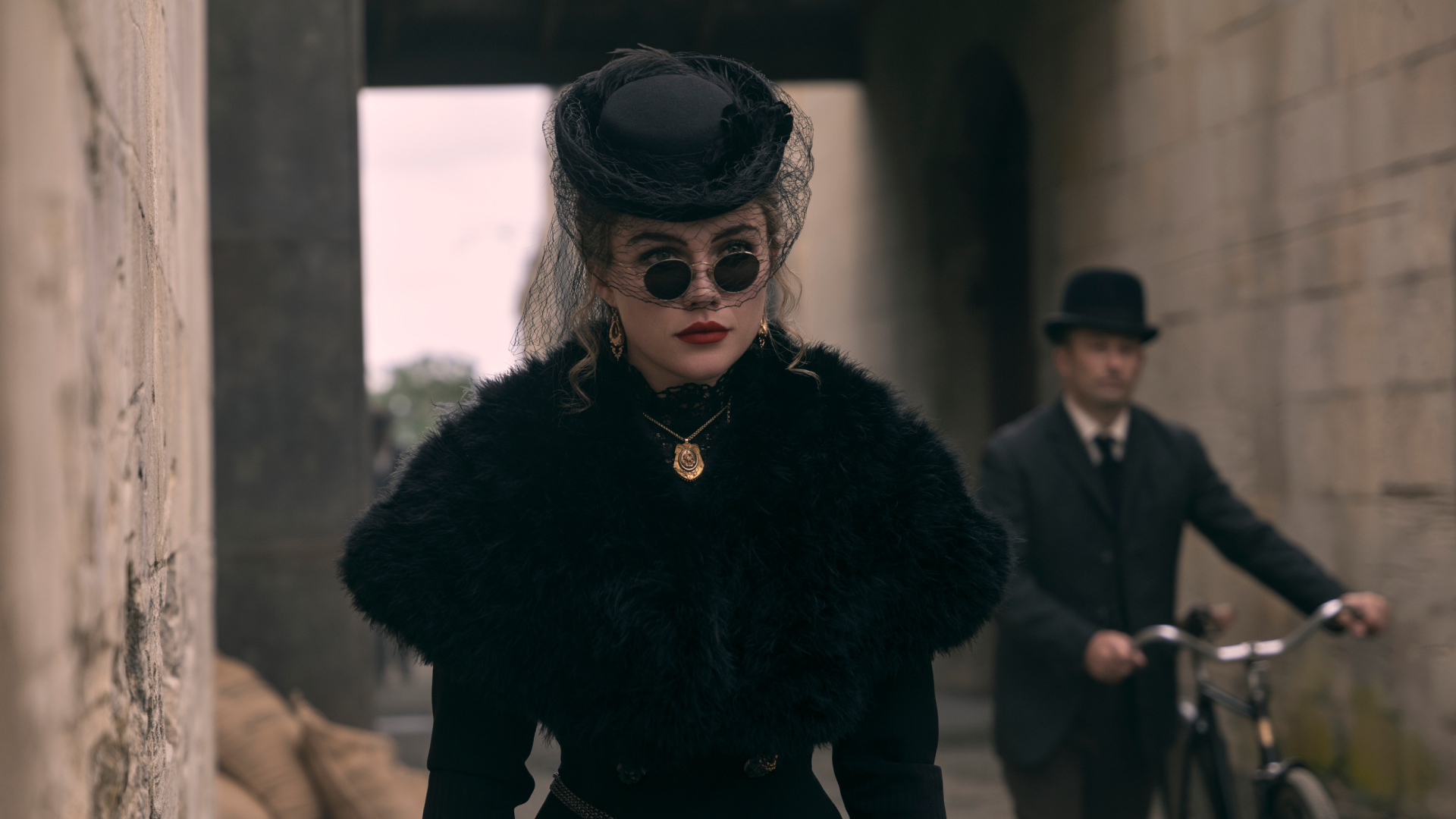 Florence Pugh as Cathy Ames waring a black gown sunglasses and hat as she walks down a street and a man with a bicycle follows her in netflix's east of eden