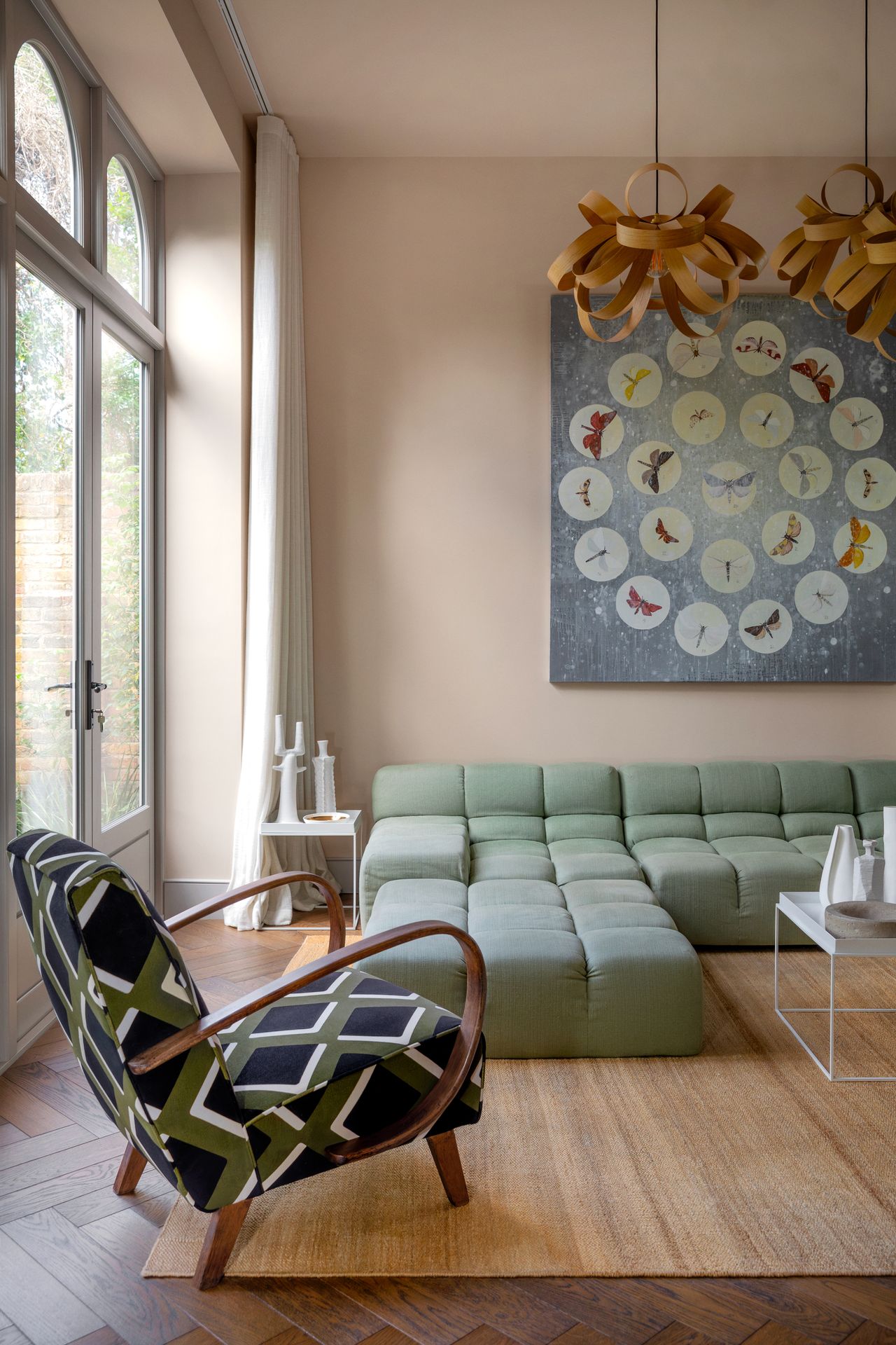 A taupe painted, modern living room with a light teal sectional sofa and a green and blue patterned accent chair.