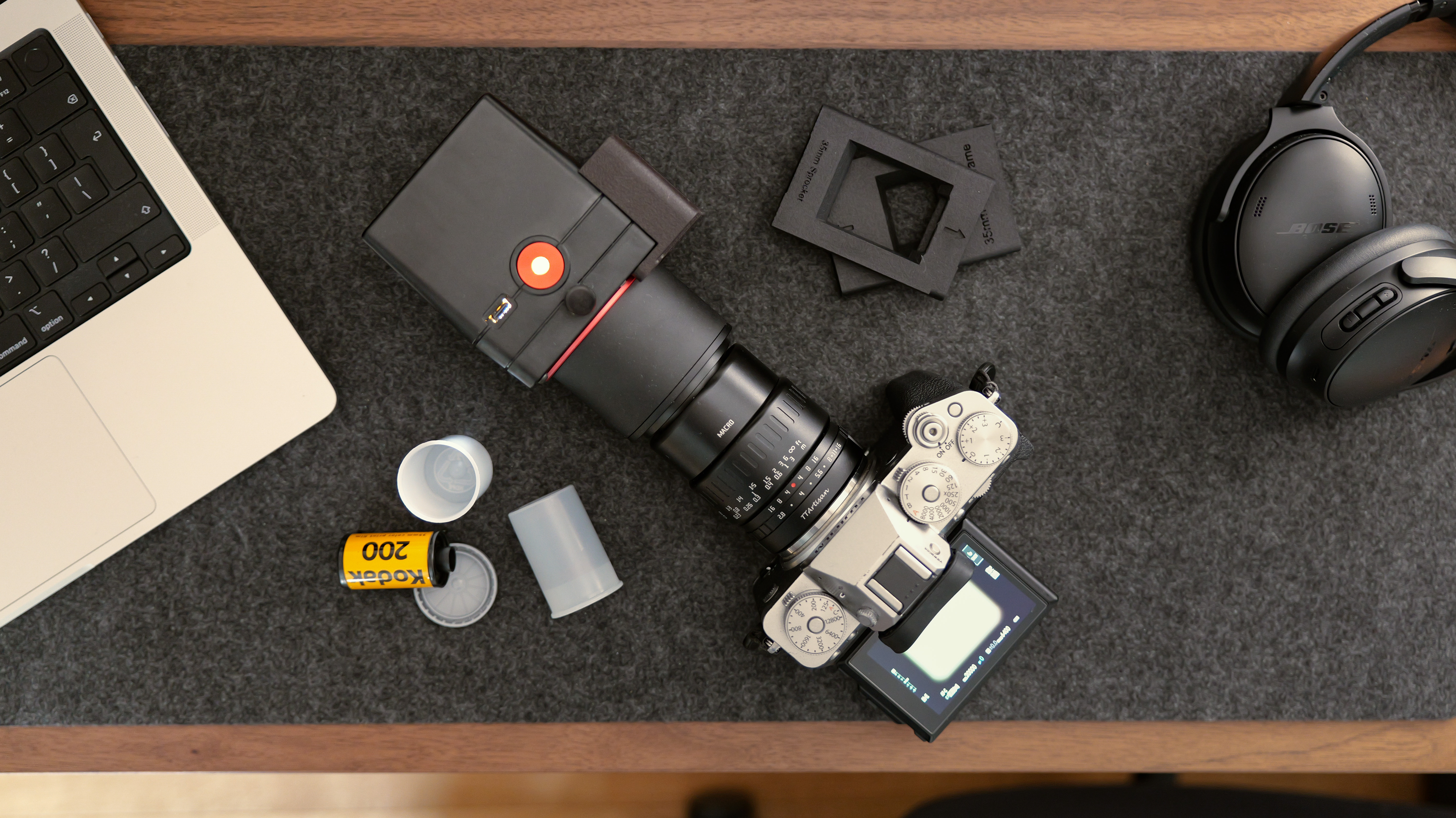 An overhead view of the Valoi easy35 V2 attached to a camera and macro lens, with film holders and a roll of Kodak 200 film on a desk.