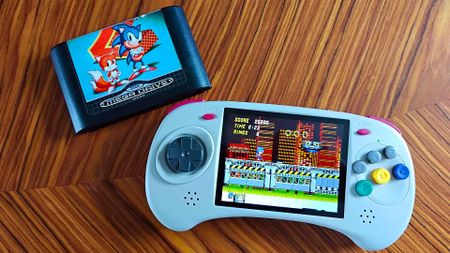 Anbernic RG ARC D handheld next to Sonic the Hedgehog 2 Mega Drive cart with gameplay on screen sitting on woodgrain table.