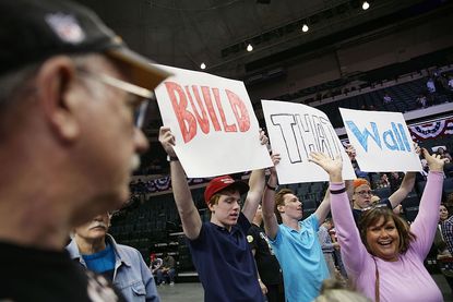 Donald Trump supporters at a rally holding "Build That Wall" signs