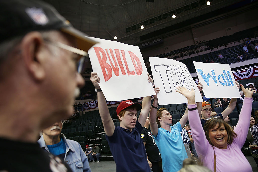 Donald Trump supporters at a rally holding "Build That Wall" signs