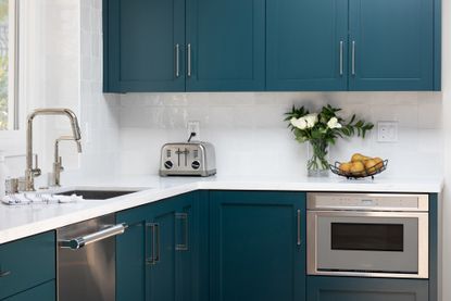 Kitchen space with teal cupboards, white countertops and backsplash