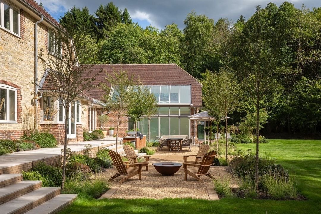 outdoor entertaining area with Adirondack chairs around a firepit on a gravel area, next to lawn, with steps up to the house