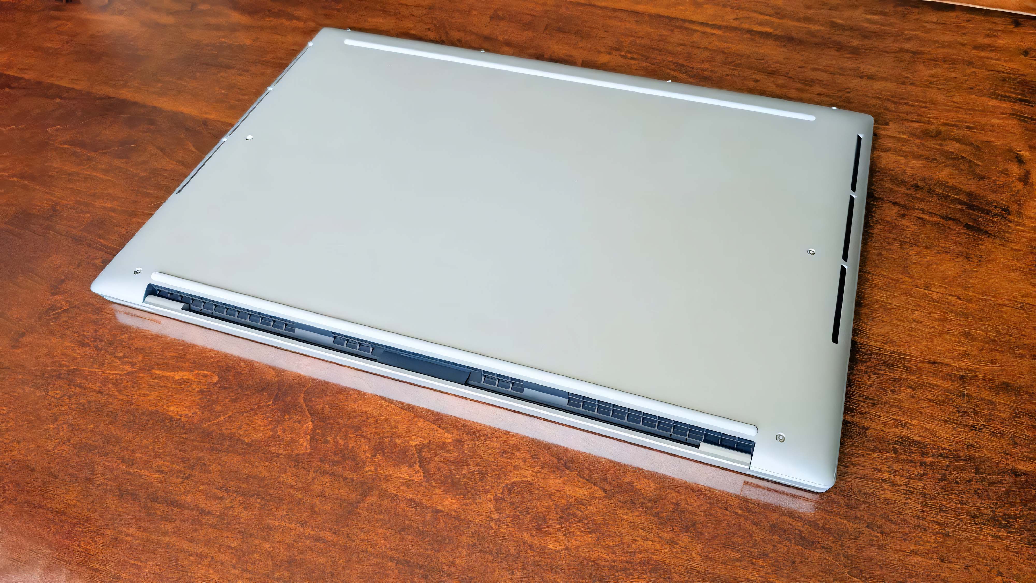 The Dell 16 Premium underside facing up on a wooden table.