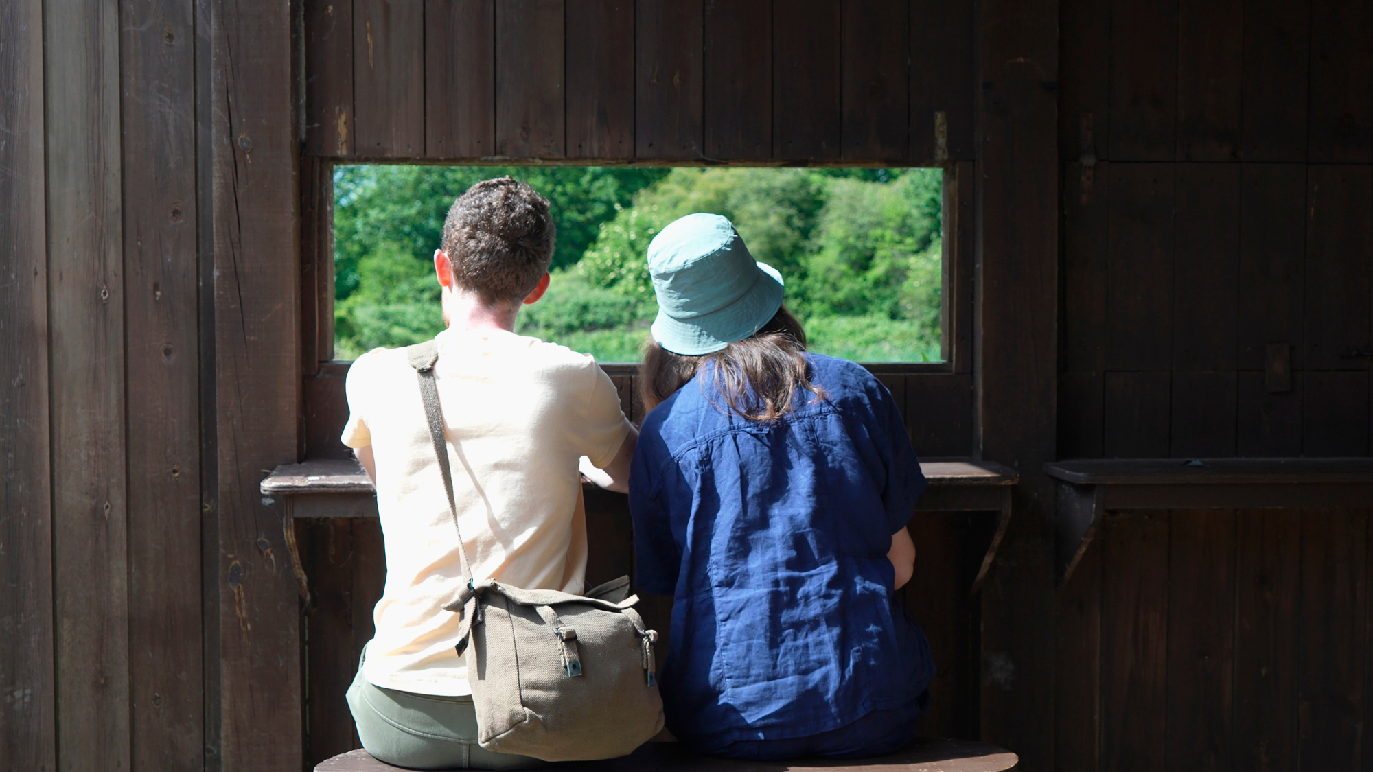 A couple of youngsters birdwatching from bird hide in nature reserve 