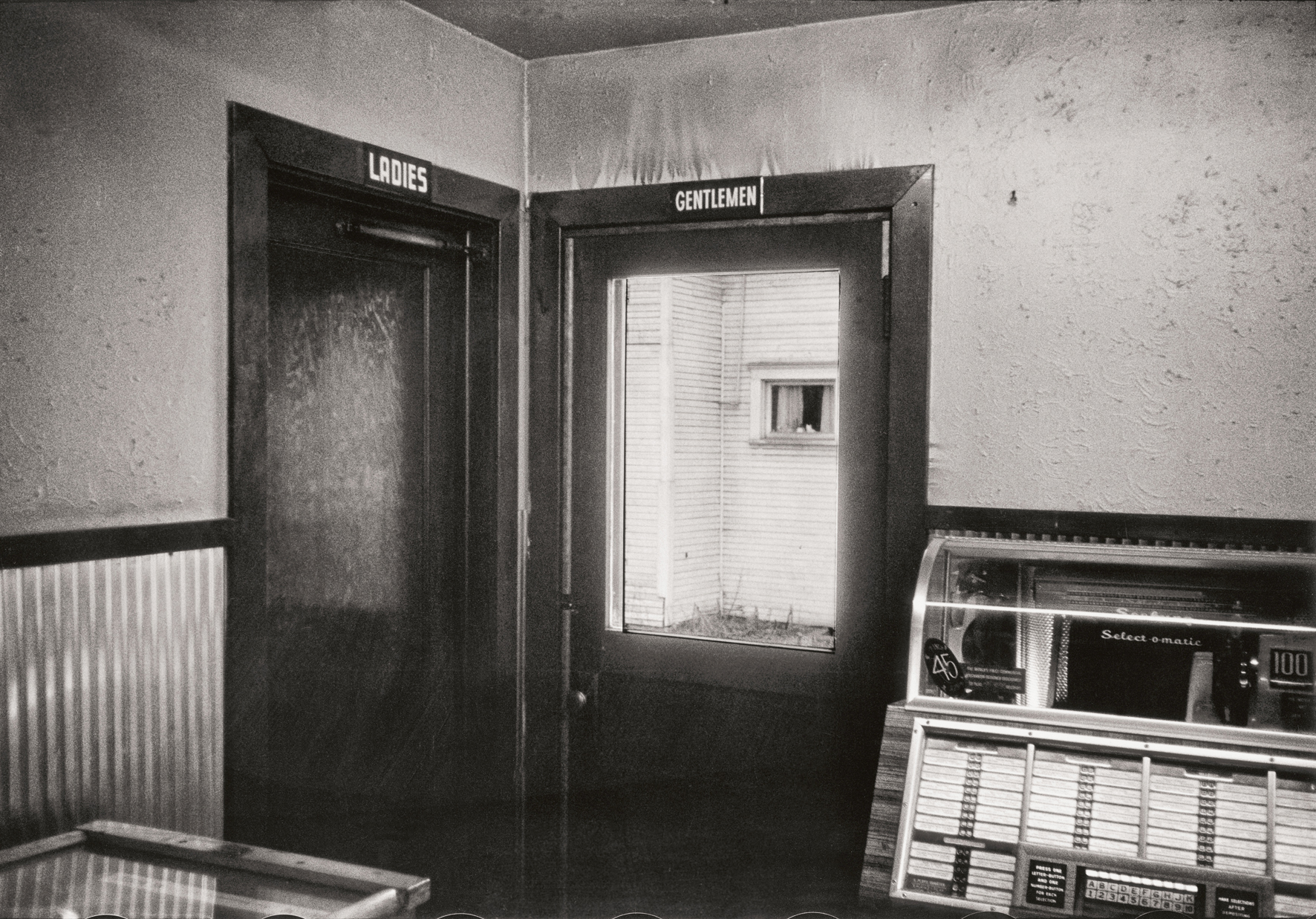 A dimly lit restroom hallway features doors labeled "Ladies" and "Gentlemen," with an old jukebox positioned nearby