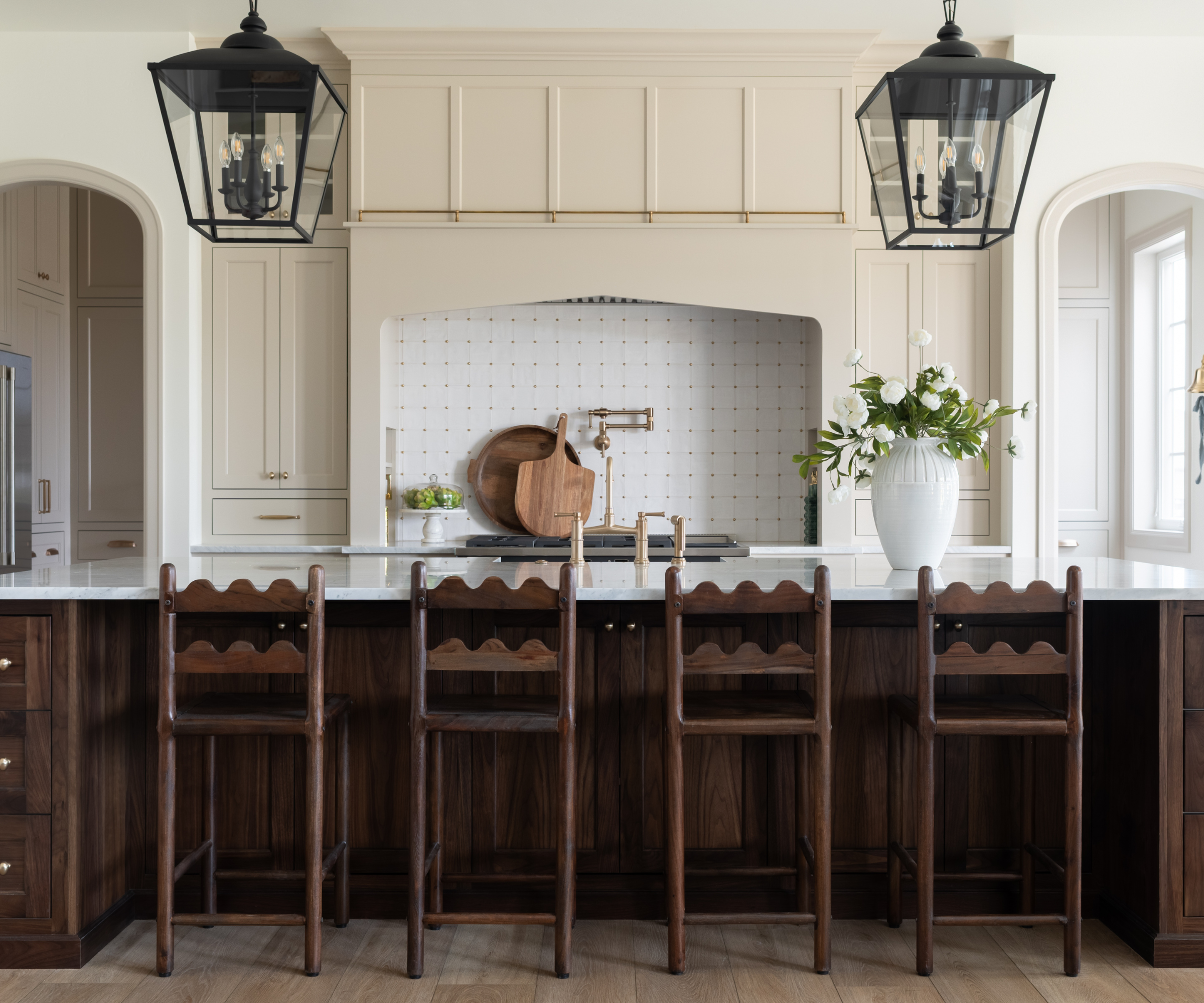 a symmetrical kitchen with wavy-back barstools, pendant lights, and a large vase of flowers on the counter