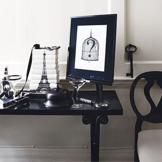 black gloss table with picture frame and black and white nick nacks beside black chair with black key on wall