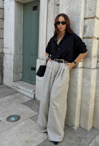 a photo showing what to wear to work in the summer with a woman wearing a black button-down shirt with tan linen trousers and black flats