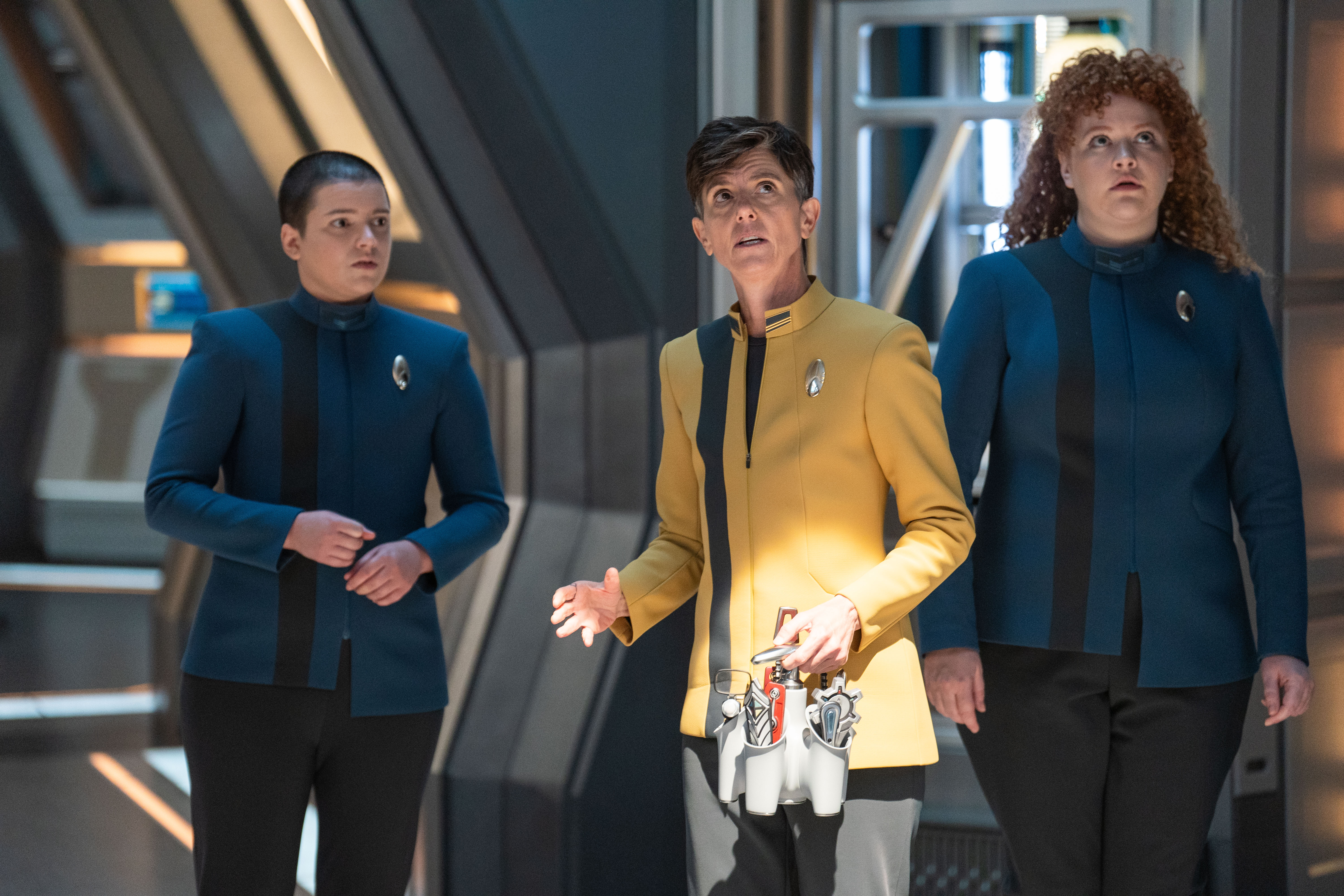 scene from a sci-fi tv show depicting three woman wearing futuristic spaceship-commander uniforms
