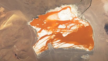 Satellite photo showing bright orange water "bleeding" across the white bed of a slat lake