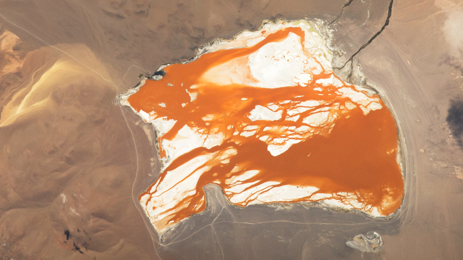 Satellite photo showing bright orange water "bleeding" across the white bed of a slat lake