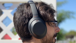 Someone wearing the Sony WH-1000XM4 wireless headphones outdoors with a white trellis and plants in the background