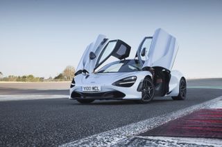 A white McLaren on a race track with its car doors open.