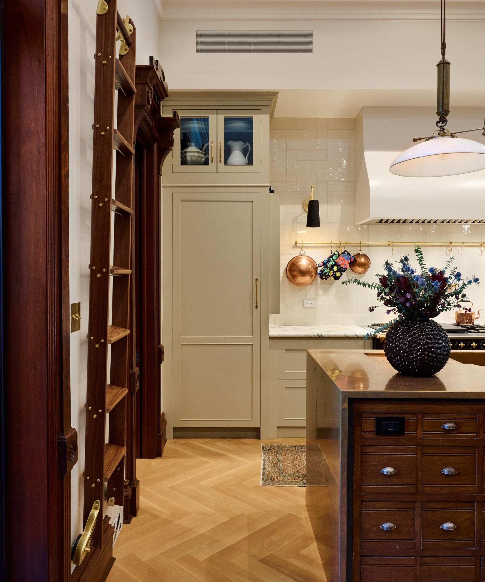 A Brooklyn Brownstone kitchen with beige cabinets, a wooden island, and a brass pot hanger on the wall