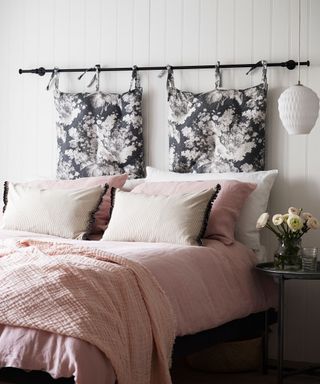 An example of guest bedroom ideas showing a bed with pink bedding and cushions, and a headboard made out of hanging cushions