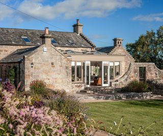 exterior or a stone coloured orangery kitchen extension on old stone detached house viewed from the garden