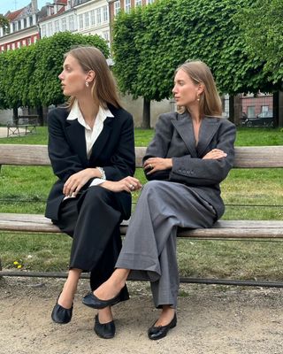 two women sitting on a bench wearing black ballet flats and pantsuits