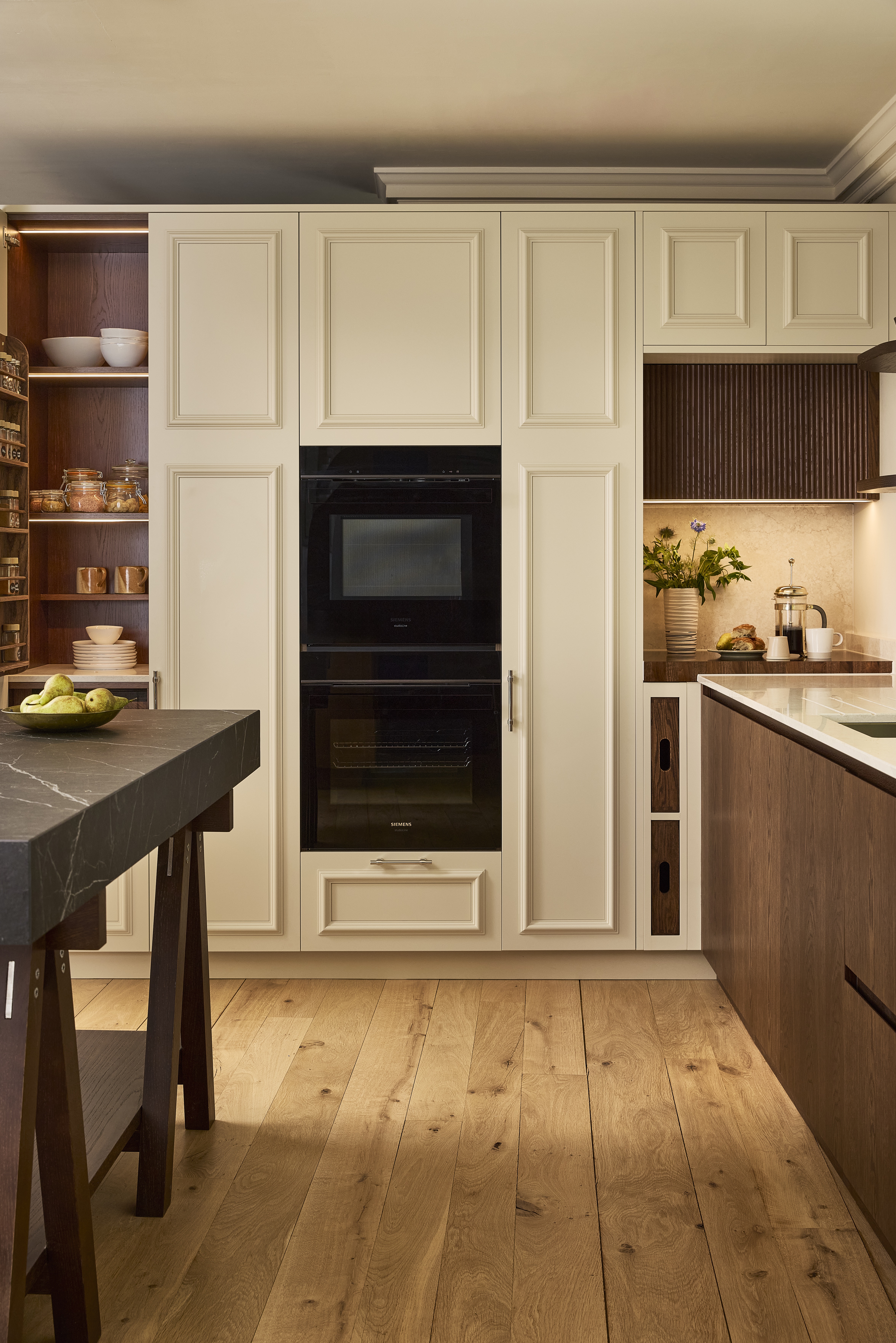 a kitchen with cream shaker cabinets, dark wooden details, a marble butchers block island and wooden flooring