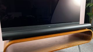 Sonos Arc Ultra on a wooden TV stand, in front of a TV