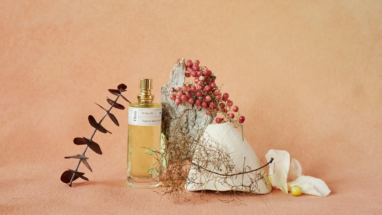 Ffern fragrance bottle on a peach background with plants