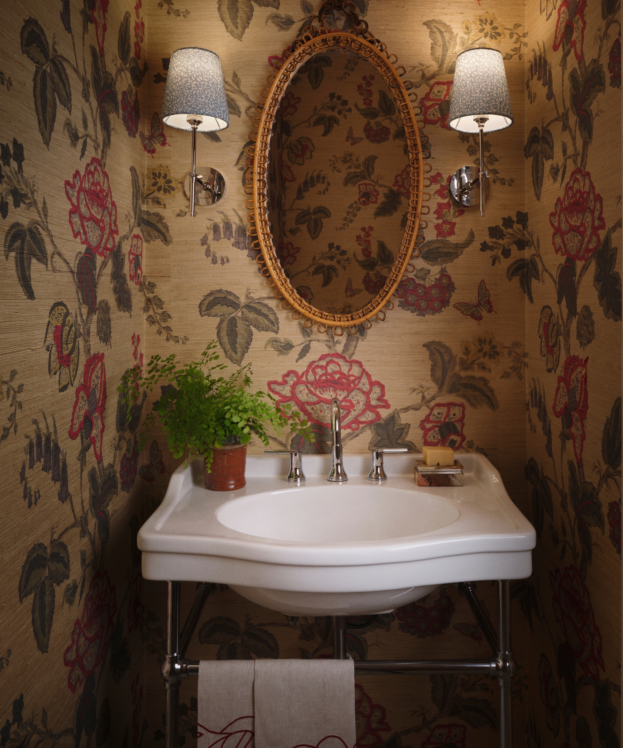 Primary bathroom with botanical grasscloth walls, white console sink, rattan mirror and patterned blue wall lights.