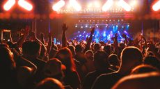 A crowd at a rock concert facing the stage with arms raised 