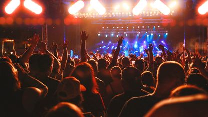 A crowd at a rock concert facing the stage with arms raised 
