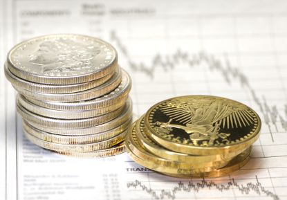 Stacks of silver and gold coins next to a stock market graph