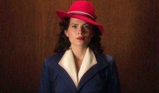 Agent Carter Hayley Atwell in a blue jacket and red hat, riding the elevator