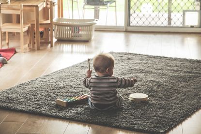 The back of a baby, sat on a rug, playing with musical instruments