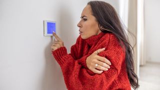 A woman with dark brown hair and wearing a red jumper turns up the heating via her smart thermostat just before going to bed, which is a big nighttime routine mistake