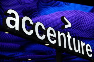 Accenture sign with white backlighting held aloft on top of a pole against a backdrop of purple graphic design denoting digitised blocks