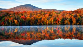 A tranquil lake in Vermont with autumn leaves and a mountain in the background
