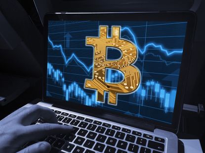 Laptop with Bitcoin B symbol on a background of financial market data in blues and orange.