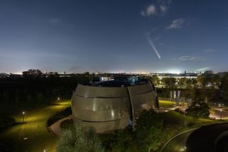 a bright white, fuzzy streak in the night sky above a large observatory dome