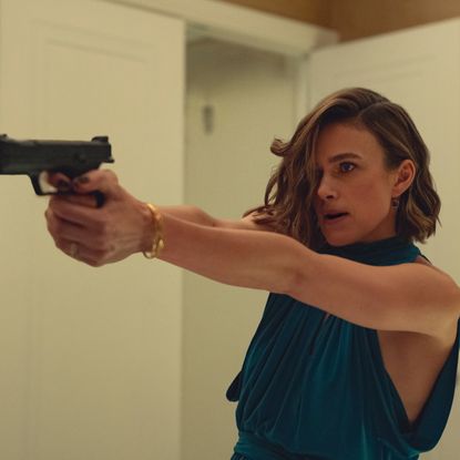 keira knightley wears a blue halter dress and points a gun in a still from black doves season 2