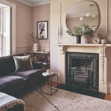 A small living room painted in pink with wall panelling, a dark velvet chaise sofa and a mirror above the fireplace