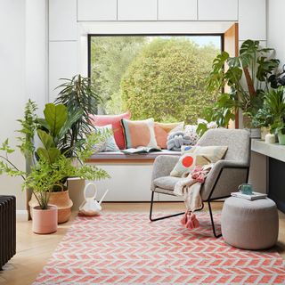 White living room with window seat covered in cushions with coral and white rug in front