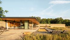exterior of meadow house, a low lying residence in the english country side featuring a flat roof and glazing inspired by modernist pavilions