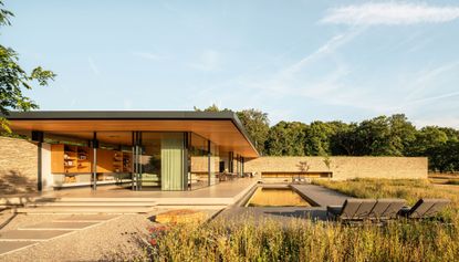 exterior of meadow house, a low lying residence in the english country side featuring a flat roof and glazing inspired by modernist pavilions